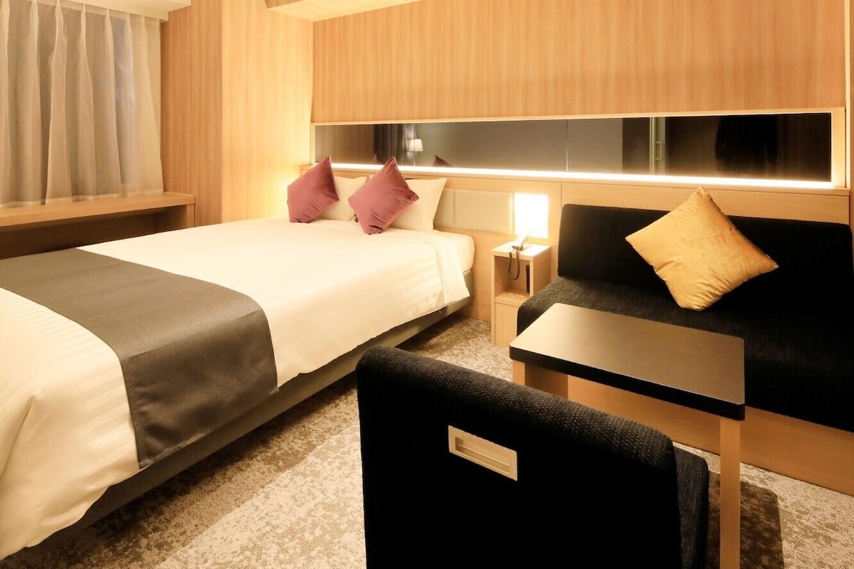 A hotel room with a bed, a sofa, a small table, and a nightstand.