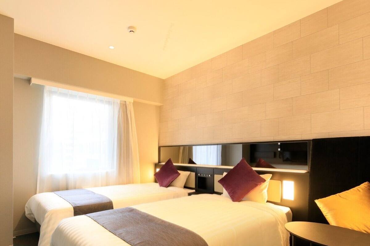 A hotel room with two beds, a TV, a small table, and a window with curtains.