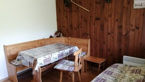 Puinen penkki, jonka päällä on kuvioitu pöytäliina, pieni puinen pöytä ja pehmustettu tuoli.
