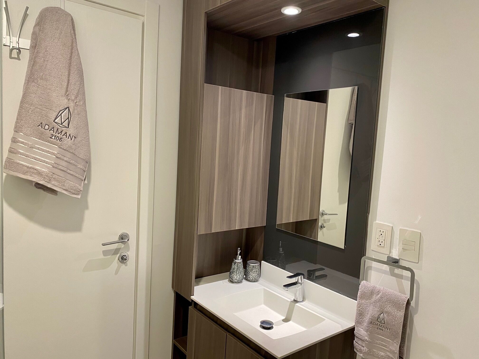 Un baño moderno con un lavamanos blanco, un espejo y dos toallas colgadas en la pared.
