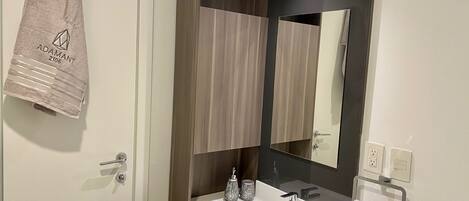 Un baño moderno con un lavamanos blanco, un espejo y dos toallas colgadas en la pared.