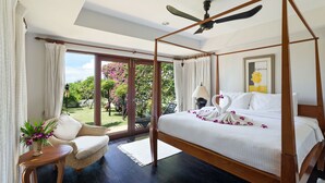A four-poster bed with a ceiling fan, a wicker chair, a small table with a plant, and a view of a garden through glass doors. - Villa Baan Hen 5 Bedroom Kata Beach (Karon)