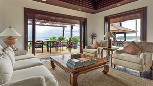 A spacious living area with a sofa, armchairs, a coffee table, and a view of the ocean through large windows. - Villa Baan Hen 5 Bedroom Kata Beach (Karon)