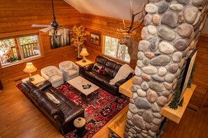 A cozy log cabin interior with a stone wall, leather furniture, and a fireplace.