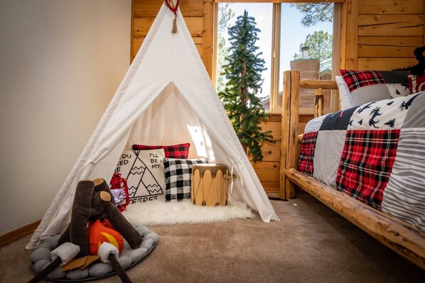 A cozy cabin room with a white tent, a bed with plaid bedding, a small drum, and a plush toy.