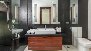 A modern bathroom with a black and white color scheme, featuring a glass-enclosed shower, a white sink with a wooden vanity, and a toilet. - Laemsingh Villa 3a 4 Bedroom in Surin (Kamala)
