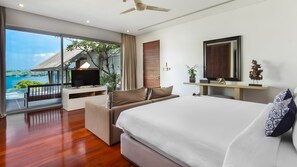 A modern hotel room with a large bed, a TV on a white console, a balcony with a view of the sea, and a wooden ceiling fan. - Laemsingh Villa 3a 4 Bedroom in Surin (Kamala)