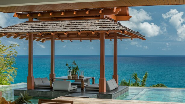 An infinity pool with a wooden deck and lounge area, overlooking the ocean. - Baan Santisuk 5 Bedroom (Kamala)