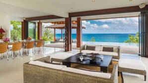 A spacious indoor area with a view of the ocean, furnished with wicker sofas, a dining table, and chairs. - Baan Santisuk 5 Bedroom (Kamala)