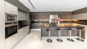 A modern kitchen with stainless steel appliances, a central island with bar stools, and a vase with flowers. - Baan Santisuk 5 Bedroom (Kamala)