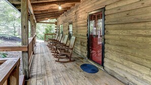 A wooden cabin with a porch, rocking chairs, and a wooden deck. - Charming Cabin with Fire Pit (Arden)