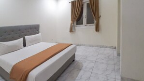 A neatly made bed with a grey headboard and white bedding, a brown throw blanket, and a window with curtains. - KoolKost Syariah near Pondok Indah Mall (Jakarta)