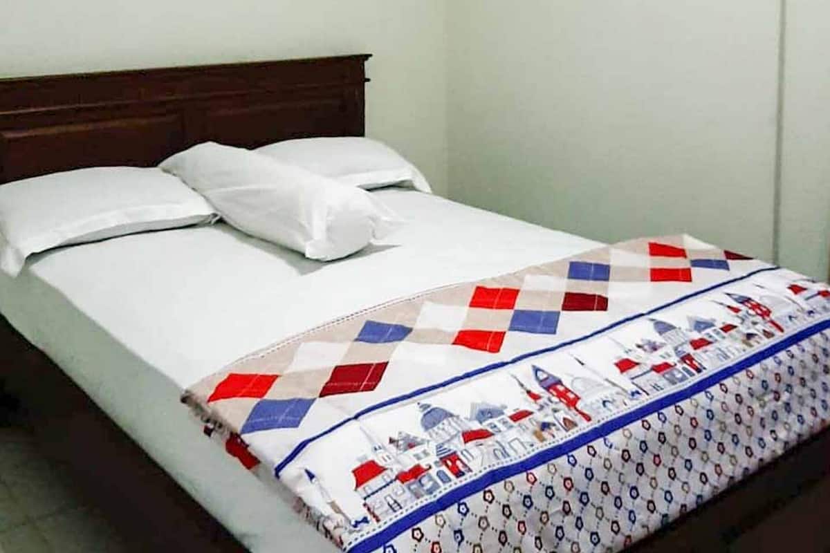 A bed with a white sheet, two pillows, and a quilt with a geometric pattern and a blue border.