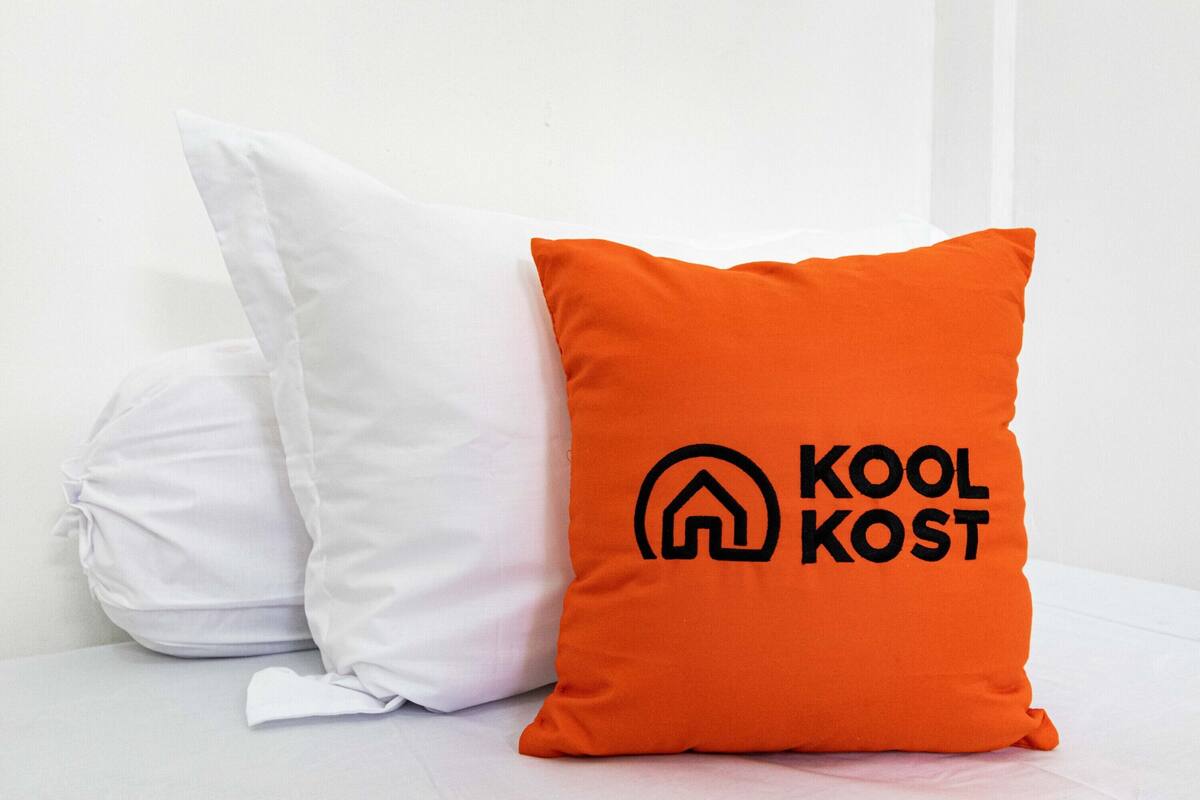 Two pillows, one white and one orange, with the orange pillow featuring a logo and text.