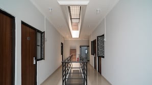 A modern hotel corridor with a central staircase, wooden doors, and a skylight.