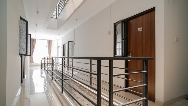 A corridor with a metal railing, a wooden door with a number, and a window with curtains.