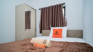 A neatly made bed with a brown blanket, a pillow with the brand name "KOOLKOST," and a towel with the number "128."