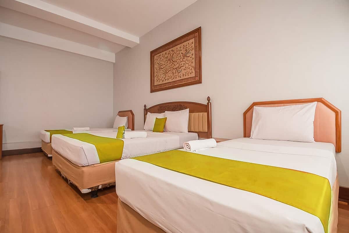A hotel room with three single beds, each with a wooden headboard, white bedding, and a green accent.