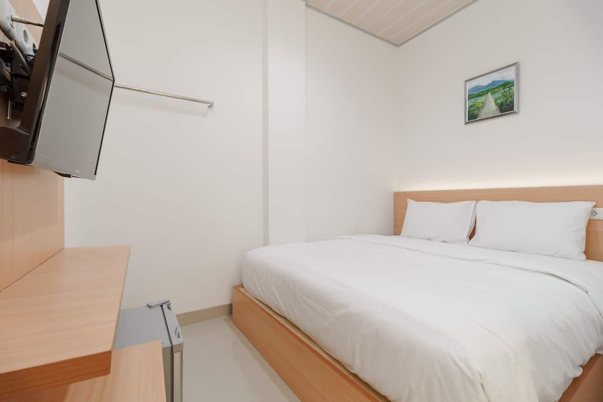 A bedroom with a bed, a wooden desk, a flat-screen TV mounted on the wall, and a painting on the wall.
