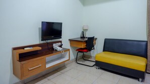 Habitació compacta amb escriptori de fusta, cadira negra, sofà groc, televisió i làmpada.