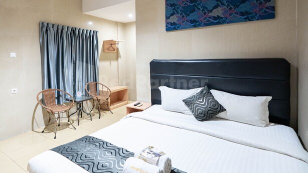 A hotel room with a bed, a desk, two chairs, a lamp, and a painting on the wall. - New Gentala Hotel RedPartner (Medan)