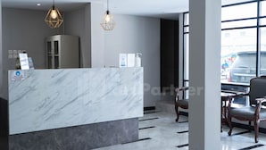 A reception area with a marble counter, two pendant lights, and a view of parked cars through large windows. - New Gentala Hotel RedPartner (Medan)