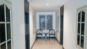 A corridor with a tiled floor, two metal chairs, a small table, and a window with a view of trees. - New Gentala Hotel RedPartner (Medan)