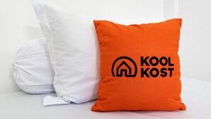 Zwei Kissen, eines weiß und eines orange mit Schrift, auf einer weißen Fläche.