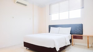 A bedroom with a bed, a bedside table, a window with blinds, and an air conditioning unit. - Waringin Residence (Medan)