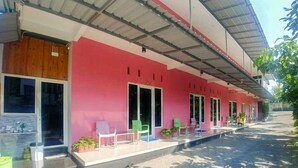 Un edificio de fachada rosa, con amplios ventanales y un área exterior cubierta con sillas y plantas en macetas.