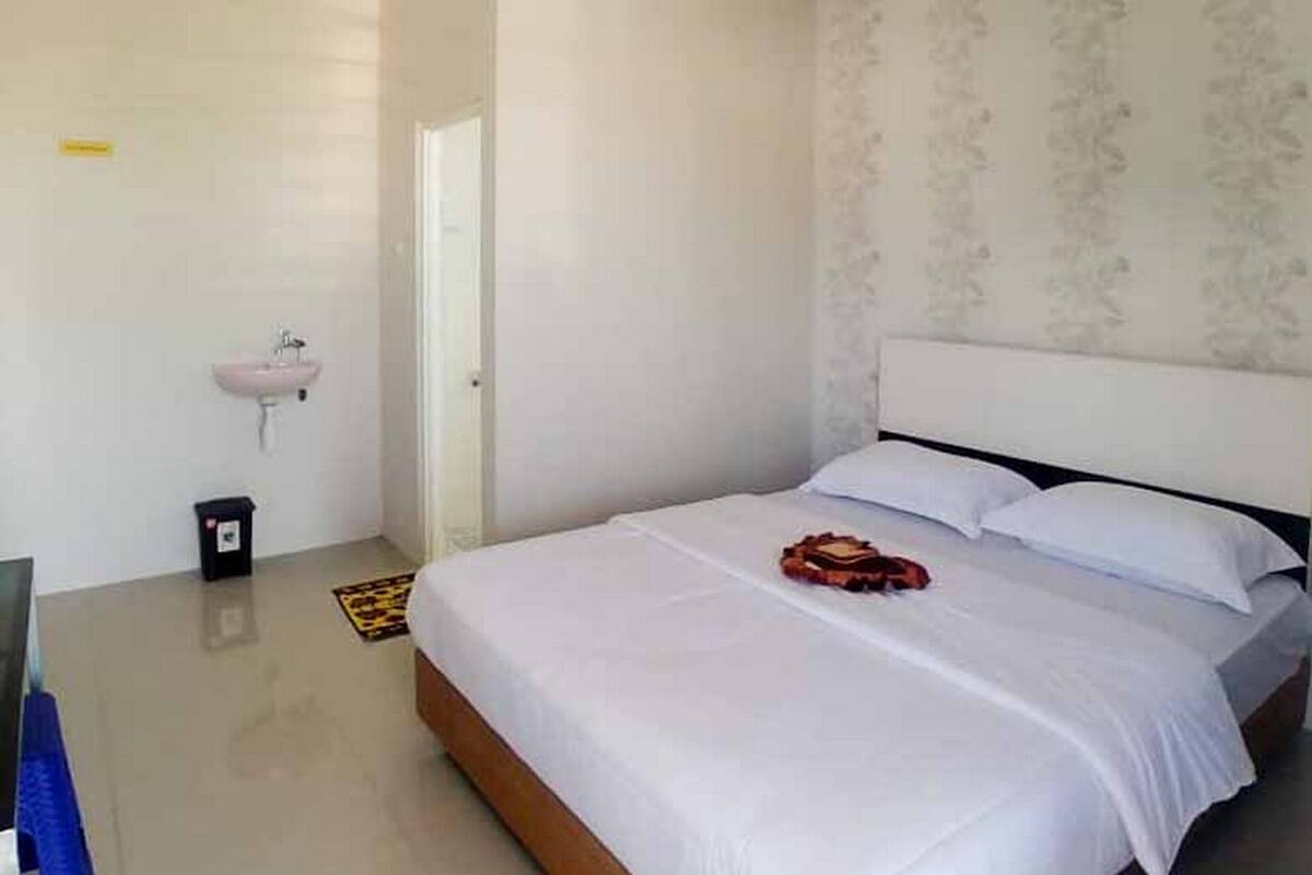Habitación de hotel con una cama individual, una mesita de noche, un lavamanos pequeño y una puerta.