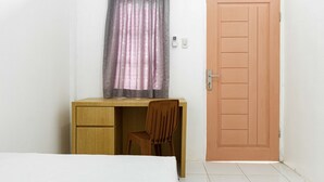 A small, simple room with a wooden desk, a chair, a bed, and a door. - KoolKost Syariah @ Taman Sentosa Cikarang (Cikarang)