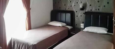 A hotel room with two single beds, a patterned wall, and a window with curtains.