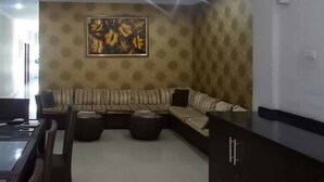 Uma sala de estar com sofá seccional, uma mesa de jantar e um quadro na parede.
