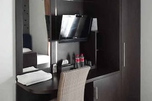 A compact hotel room with a bed, a small table with a chair, a flat-screen TV mounted on the wall, and a minibar. - RedDoorz near Pantai Panjang Bengkulu 2 (Bengkulu)
