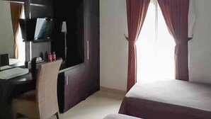 Quarto de hotel com uma cama, uma escrivaninha com cadeira, televisão e janela com cortinas.