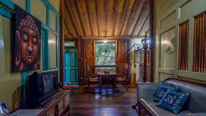 A traditional room with a wooden ceiling, a dining table with chairs, a sofa with cushions, and a Buddha statue on the wall. - Upala Java Huise (Bangunjiwo)