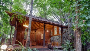 A wooden cabin with a porch, surrounded by lush greenery. - Upala Java Huise (Bangunjiwo)
