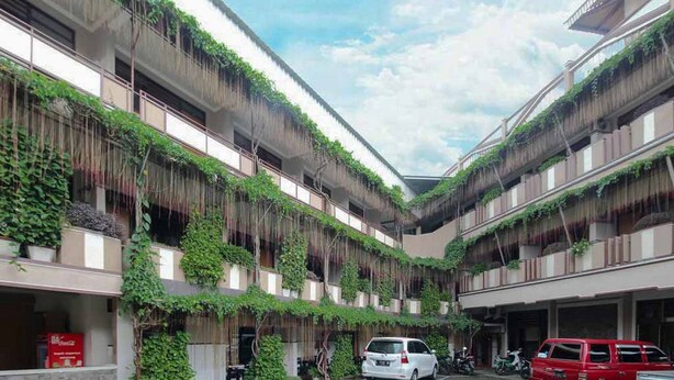 A multi-story building with balconies covered in greenery, a central open space, and parked cars. - Hotel Lestari Near Lippo Plaza Mall Jember (Patrang)