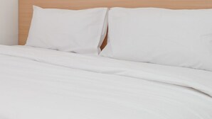 A bed with white bedding and a wooden headboard. - Hotel Lestari Near Lippo Plaza Mall Jember (Patrang)