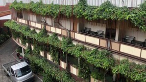 A building with multiple balconies covered in greenery, a parked vehicle, and outdoor seating. - Hotel Lestari Near Lippo Plaza Mall Jember (Patrang)