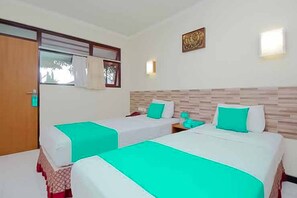 A hotel room with two beds, each with a white bedspread and teal accents, a wooden headboard, a wall-mounted artwork, and a window with curtains. - Hotel Lestari Near Lippo Plaza Mall Jember (Patrang)