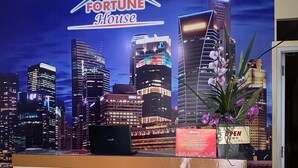 A reception desk with a laptop, a 'Fortune House' sign, and a 'OPEN' sign in a cityscape backdrop. - RedDoorz @ Jalan Morotai Lampung (Bandar Lampung)