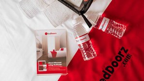 A promotional display for RedDoorz.com featuring a bed, a RedDoorz branded bag, and a RedDoorz water bottle. - RedDoorz @ Jalan Morotai Lampung (Bandar Lampung)