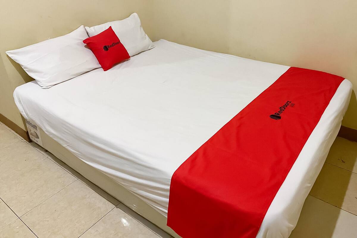 A single bed with a white mattress and a red blanket.