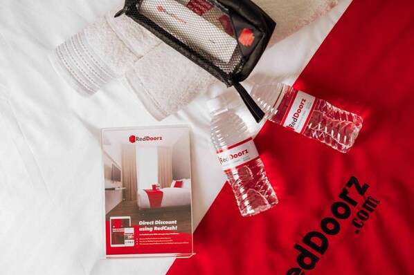 Une présentation promotionnelle pour RedDoorz.com comprenant un lit, un sac de la marque RedDoorz et une bouteille d’eau RedDoorz.