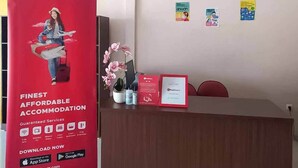 Un comptoir d'accueil orné d'une publicité pour RedDoorz, d'une orchidée en pot et d'un certificat encadré.