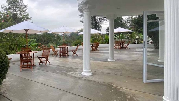 An outdoor patio area with wooden chairs and tables, white columns, and umbrellas.