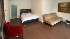 A modern hotel room with a bed, a sofa, and a red chair.