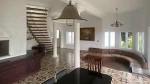 A spacious living room with a black dining table, a brown leather sofa, and a staircase leading to another level.